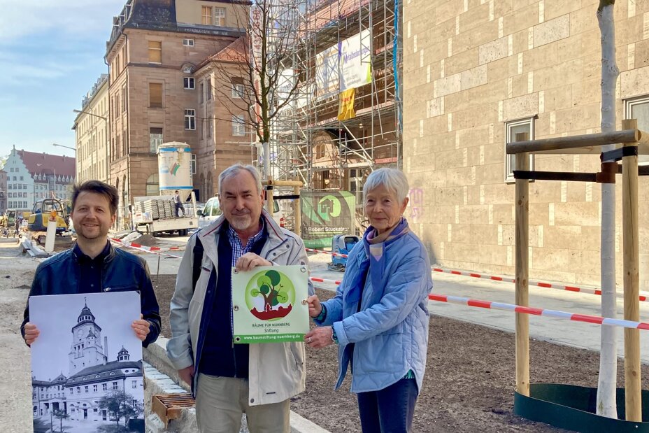 Von links: Baummanager vom Servicebetrieb Öffentlicher Raum Nürnberg, Florian Demling, sowie die Vertreter der „Bäume für Nürnberg Stiftung“, Vorstandsvorsitzender Mathias Schmidt und Stiftungsgründerin Margit Grüll, vor dem Volksbad Nürnberg mit den beiden von der Stiftung gespendete Bäumen im Hintergrund.