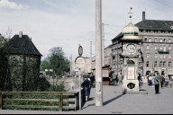 Bild Ein Relikt aus längst vergangenen Zeiten: das Uhrenhäuschen am Bahnhofsplatz. Das Schild im Vordergrund weist den Weg in die Altstadt, der – wie auch heute noch – durch den Waffenhof führt. Dieser ist eigentlich der Vorhof des Königs- und Frauentorzwingers und seit 1971 als Handwerkerhof eine touristische Attraktion. Foto Hochbauamt, Mai 1959. (StadtAN A 55 Nr. II-3-36)