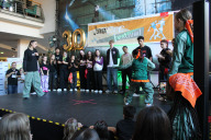 Bild 30 Jahre Junior-Dance-Festival: zwei Finalistinnen des Dancebattles , die gegeneinander tanzen. Im Hintergrund sind alle Teilnehmenden mit drei Jurymitgliedern, im Vordergrund Kinder und Jugendliche, die beim Battle zuschauen, zu sehen. 