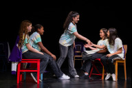 Bild „Mosaik-­Jugendpreis – Mit Vielfalt gegen Rassismus“ 2026: Das Nürnberger Schultheaterprojekt „Das was fehlt – Eine Übung im gemeinsamen Erinnern“ der Scharrer­-Mittelschule hat den 2.Preis erhalten. Die Schülerinnen der Scharrer-Mittelschule (v. li.) Audrey, Sophia, Astera, Mascha und Leticia verwandeln die Stühle auf der Bühne in eine U-Bahn. 