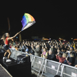 Künsterlin mit einer Pride-Flagge und jubelndem Publikum