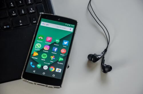 Smartphone mit verschiedenen Apps auf der Tastatur eines Laptops liegend; daneben befinden sich Kopfhörer