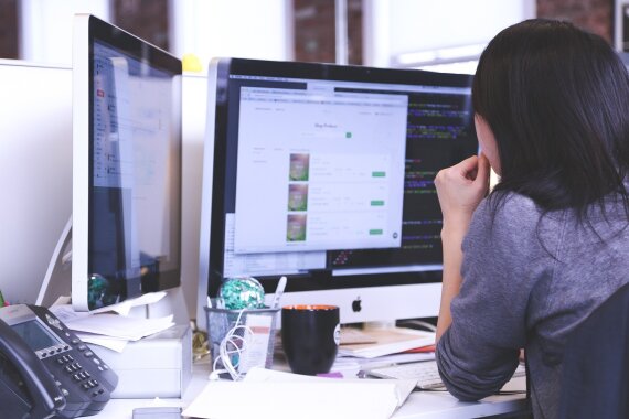 Frau während der Arbeit im Büro vor zwei Monitoren sitzend