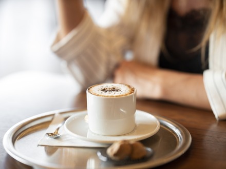 Foto von einer Tasse Kaffee auf einem Tablett. Das Tablett steht auf einem Tisch. Am Tisch sitzt eine Frau., Bild © www.pixabay.com