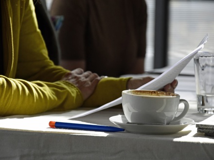 Das Bild zeigt: Ein Mensch liest bei einer Tasse Kaffee etwas vor.