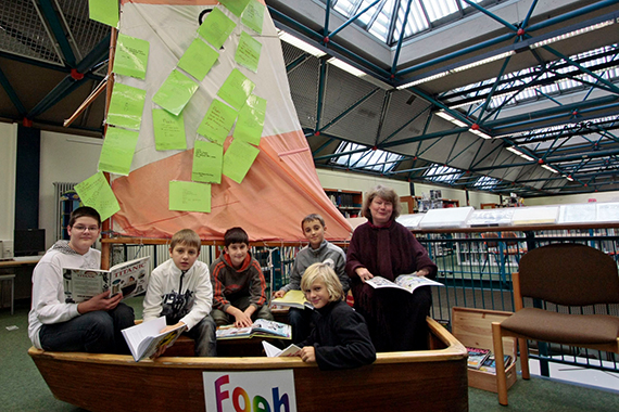 Kinder mit Büchern in einem Holzboot in der Bibliothek