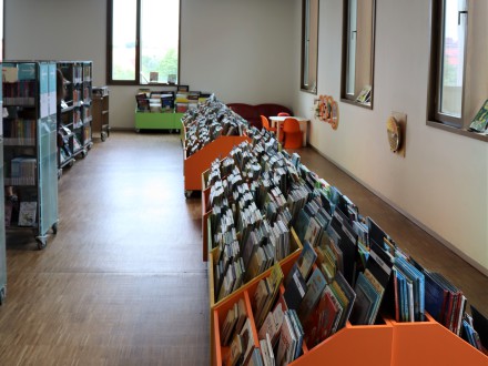 Das Bild zeigt ein paar Regale in der Kinder·bibliothek. Rechts im Bild sind niedrige Regale mit Bilder·büchern. Links im Bild sind Regale mit Büchern.