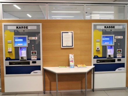 Auf dem Bild sind 2 Bezahl·automaten. Die Bezahl·automaten sind in der Wand eingebaut. Zwischen den Bezahl·automaten steht ein kleiner Tisch an der Wand.