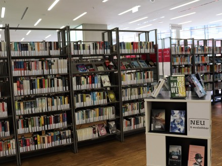 Das Bild zeigt einen Raum mit vielen Bücher·regalen. Im Vordergrund steht ein Info-Tisch mit neuen Büchern.