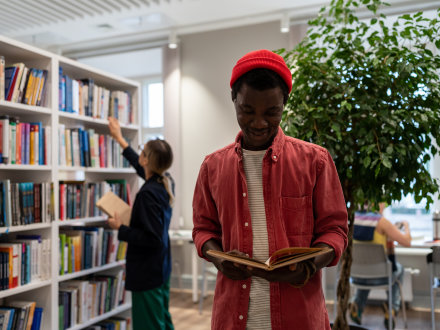 Das Bild zeigt: Ein junger Mann steht mit einem offenen Buch in den Händen da. Der junge Mann liest in dem Buch.