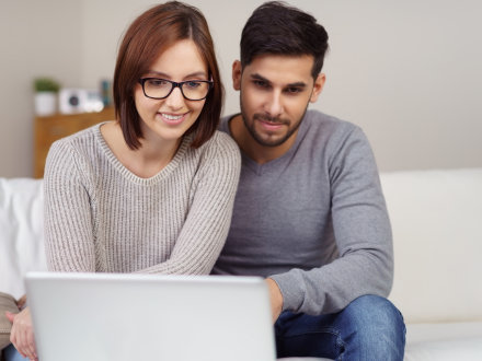 Das Bild zeigt: Eine Frau und ein Mann schauen zusammen auf den Bildschirm von einem Laptop.