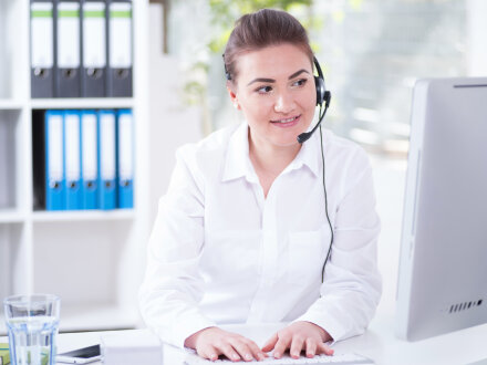 Foto von einer Frau in einem Büro. Die Frau telefoniert gerade über einen Kopf·hörer.