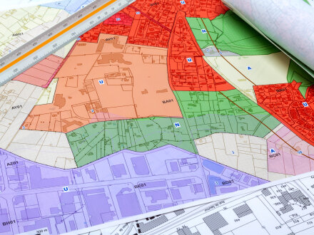 Das Bild zeigt einen Flächen·nutzungs·plan. Der Flächen·nutzungs·plan zeigt verschiedene Flächen in einem Gebiet. Die Flächen sind als bunte Abschnitte gekennzeichnet. Ein Lineal liegt auf dem Flächen·nutzungs·plan. Unter dem  Flächen·nutzungs·plan ist noch ein kleiner Teil von einem anderen Plan zu erkennen.