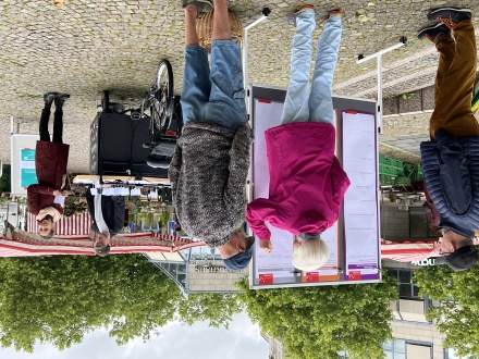 Foto von einem Info-Stand von der Abteilung Stadt·erneuerung. Der Info-Stand ist draußen auf einem Platz. Eine Frau schreibt gerade etwas auf ein Plakat.