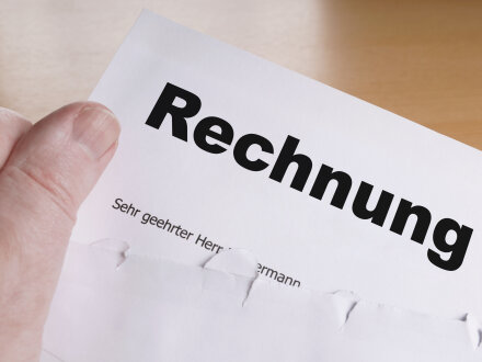 Foto von einem Brief mit einer Rechnung. Eine Hand zieht gerade die Rechnung aus dem Brief·umschlag.