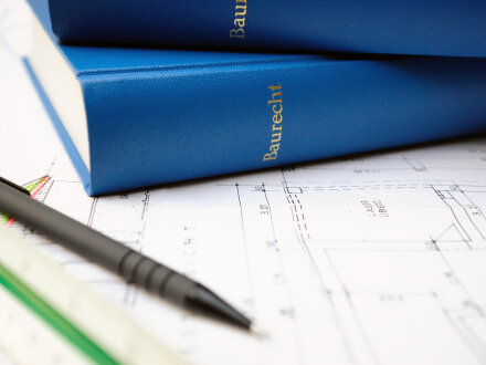 Auf einem gezeichneten Bau·plan liegen 2 blaue Bücher über·einander. Auf dem Buch·rücken steht auf beiden Büchern: Bau·recht. Vor den Büchern liegen ein Stift und ein Lineal.