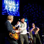 Drei Musiker auf der Bühne vor einem Nuejazz-Plakat.