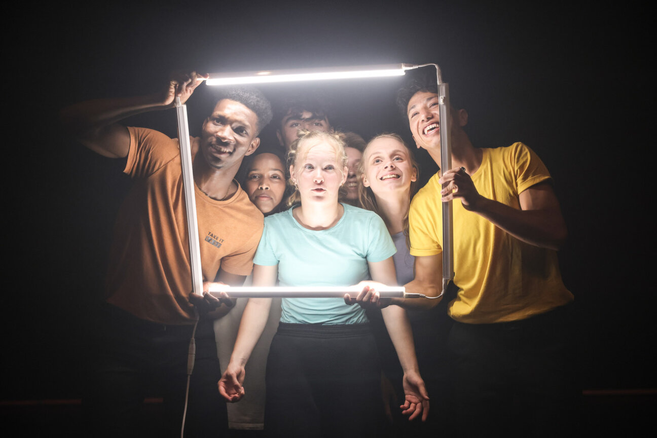 Jugendliche Schauspielende von Dramaclλn aus der Manufactur Herford schauen durch einen Rahmen aus LED-Röhren, Bild © Dave Grossmann
