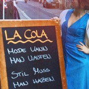 Ein Schild steht vor dem Secondhandladen mit der Aufschrift "La Cola. Mode kann man kaufen, Stil muss man haben."