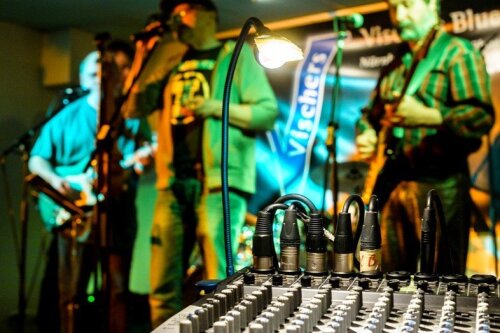 Musiker auf einer Bühne, hinter einem Mischpult, welches im Fokus steht © Uwe Niklas