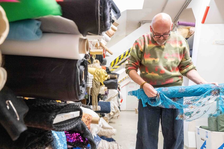Gunther Bickel im Stofflager der Damenschneiderei des Staatstheaters Nürnberg. Er hält eine blaue Stoffrolle.