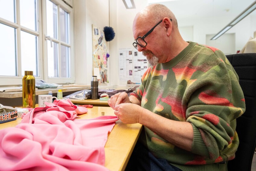 Gunther Bickel in der Damenschneiderei im Theater Nürnberg. Er näht von Hand an einem pinken Rock.