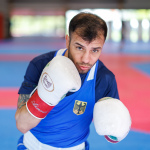 Foto: Boxer Omid Ahmadisafa blickt in Kampfhaltung in die Kamera, dabei trägt er weiße Boxhandschuhe.