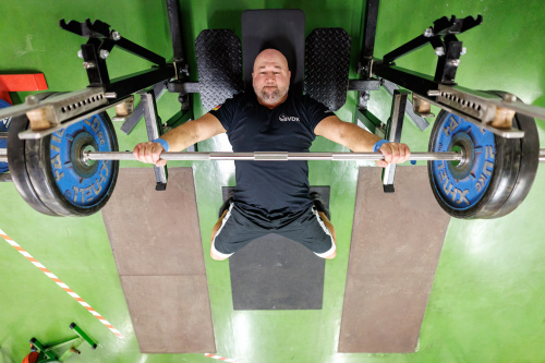 © Daniel Karmann Foto: Blick von Oben auf den Kraftsportler Thomas Ziegler, der auf einer Bank liegend eine Langhantel nach oben drückt. © Daniel Karmann