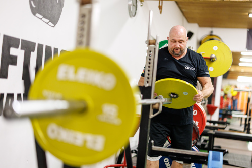 Foto: Kraftdreikämpfer Thomas Ziegler steckt eine gelbe 15 kg Scheibe auf eine Langhantel.