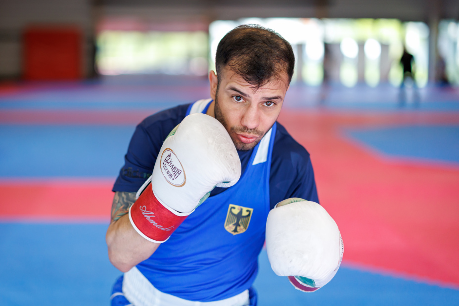Foto: Boxer Omid Ahmadisafa blickt in Kampfhaltung in die Kamera, dabei trägt er weiße Boxhandschuhe.