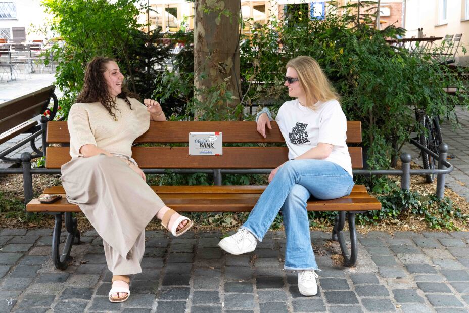 Bild © Christine Dierenbach / Stadt Nürnberg Foto: Zwei junge Frauen auf einer Parkbank unterhalten sich. Dazwischen an der Rückenlehne ein Schild "Plauderbank"., Bild © Christine Dierenbach / Stadt Nürnberg