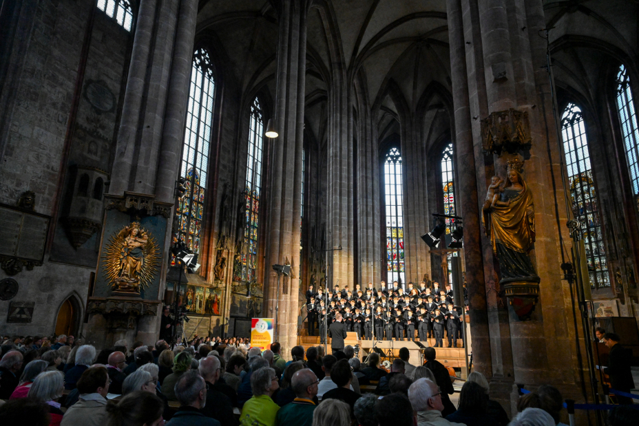 Foto: Der Innenraum einer gotischen Kirche. Im Hintergrund ein Chor auf einem Podest, im Vordergrund Besucher in den Kirchenbänken von hinten., Bild © Christine Dierenbach / Stadt Nürnberg