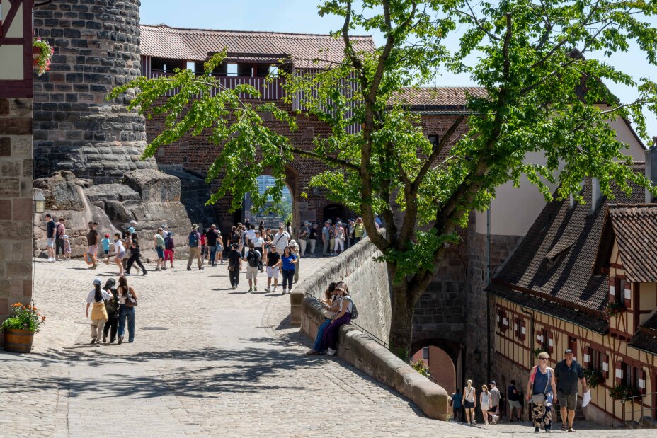 Foto: Blick auf die Außenanlage der Kaiserburg. Sandstein und Fachwerkgebäude sowie Gruppen von Besucherinnen und Besuchern., Bild © Stadt Nürnberg/Christine Dierenbach