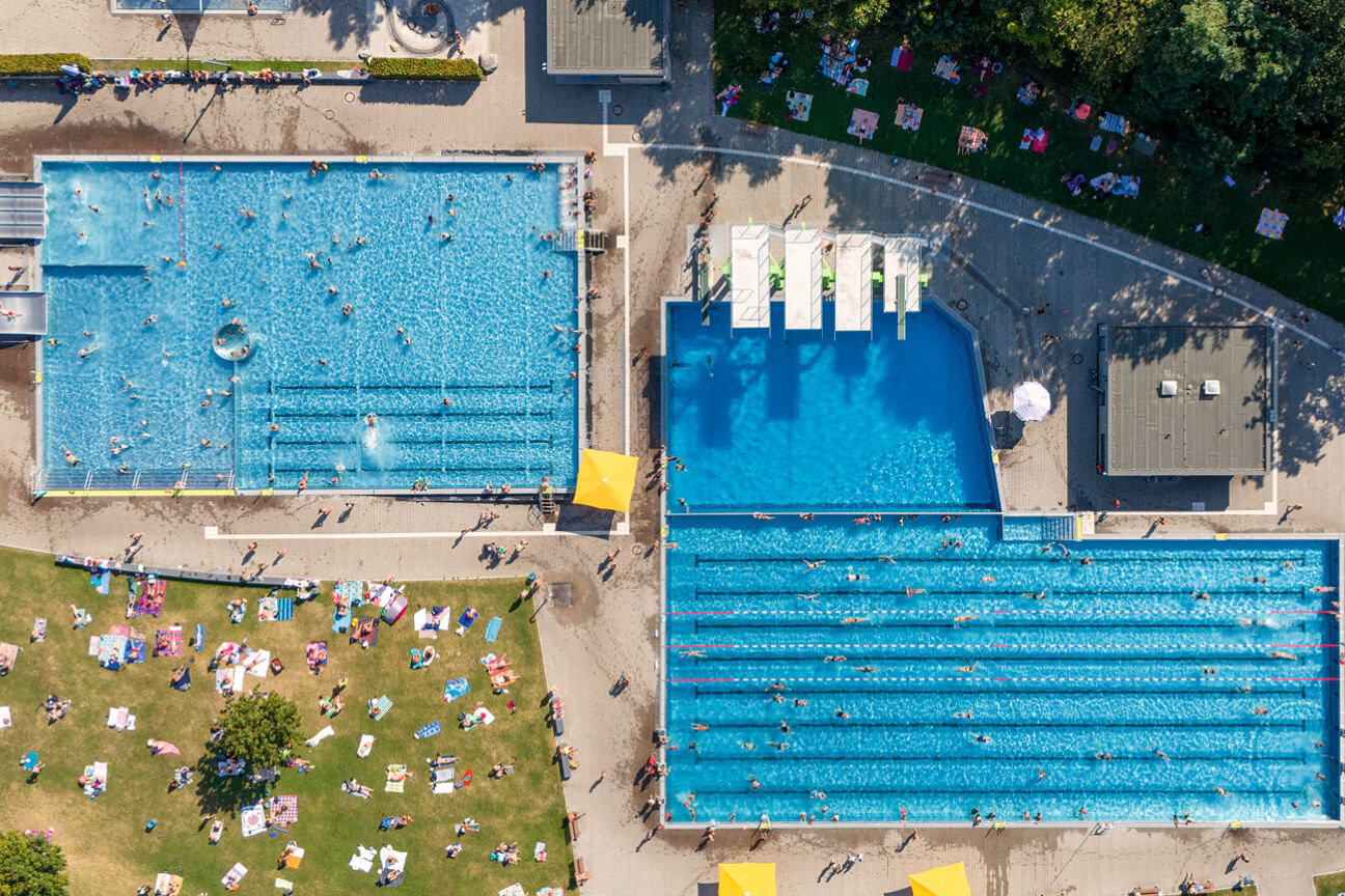 An heißen Sommertagen bilden im Westbad die Handtücher der Gäste auf der grünen Wiese einen bunten Flickenteppich, während in den Becken die Schwimmerinnen und Schwimmer ihre Bahnen ziehen., Bild © Marius Marthold / Stadt Nürnberg