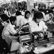 Asiatische Arbeiterinnen in einer Fabrikhalle an Maschinen.