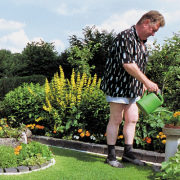 Ein Mann steht auf seinem gepflegten Rasen und gießt eine Blume.