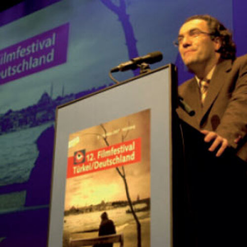 © Bernd Böhner Festivalchef Adil Kaya steht am Redepult mit Mikrofon und eröffnet die interkulturellen Filmfestspiele, © Bernd Böhner