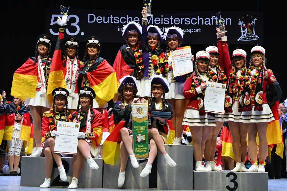 Bild © Manfred Ruff Foto: Junge Frauen in Gardetanzuniformen auf einem Siegerpodest halten Siegerurkunden in der Hand. Um die Schultern haben sie schwarz.rot-goldene Flaggen gelegt., Bild © Manfred Ruff