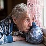 Eine betagte Dame sieht traurig aus dem Fenster