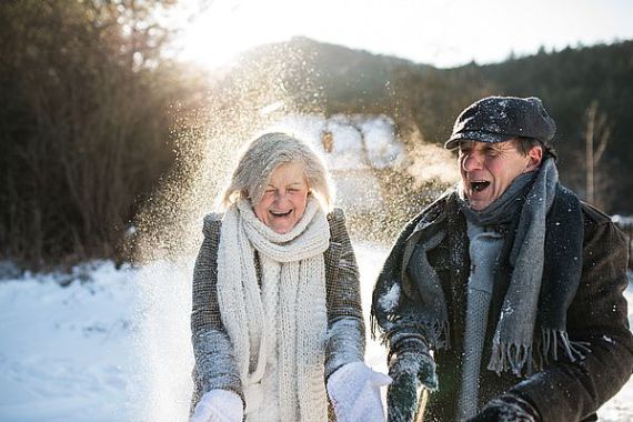 Beautiful senior couple blowing snow in sunny winter nature