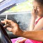 Kind hält im Auto neben einem rauchenden Erwachsenen die Nase zu