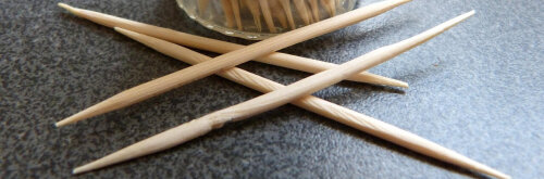 Zahnstocher liegen auf einem Tisch vor einem vollem Glas mit Zahnstochern