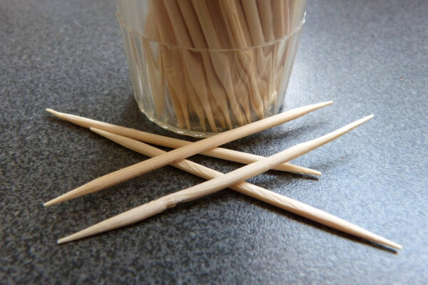 Zahnstocher liegen auf einem Tisch vor einem vollem Glas mit Zahnstochern