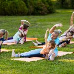 Group of mothers and their children doing exercise practicing yoga on a fitness rugs on the fresh air