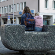 Rückenblick zweier jungen Frauen die nebeneinander auf einem Skulptur sitzen