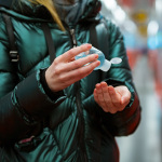Eine Frau in Winterjacke desinfiziert ihre Hände.