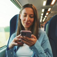 Eine junge Frau liest auf ihrem Smartphone während sie mit einer Regionalbahn durch eine Landschaft fährt.