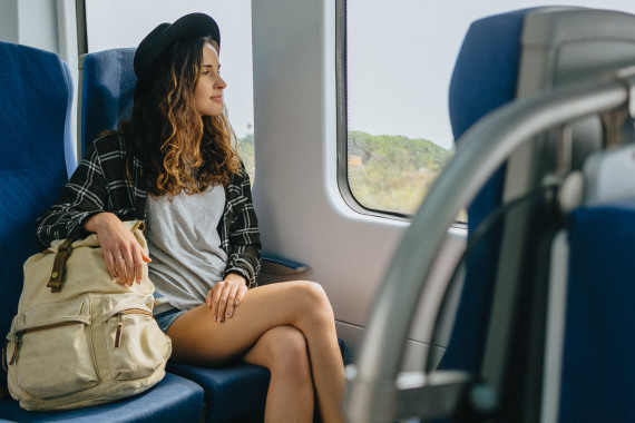 Eine Frau mit einem Wanderrucksack sitzt im Zug und sieht aus dem Fenster.