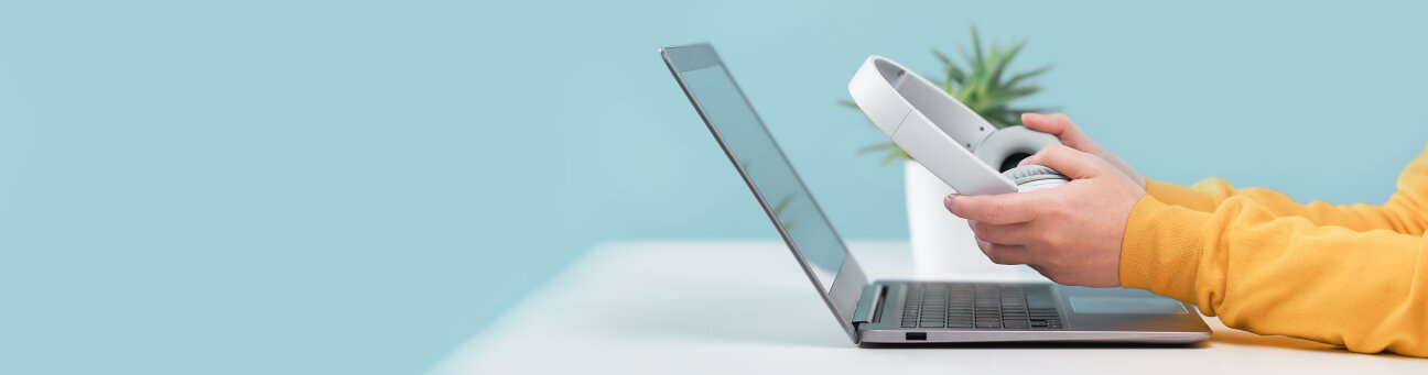 Person hält Kopfhörer in der Hand und blickt auf den Laptop, Bild © AdobeStock