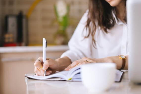 Close up of a woman writer hand writing in a notebook at home in the kitchen